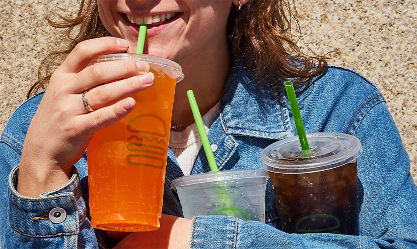Woman holding three sodas in Shake Shack cups with one lifted to her lips. 